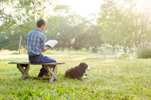 a man reading a Bible outdoors with his dog