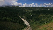 aerial view over a bridge and highway through green mountains 