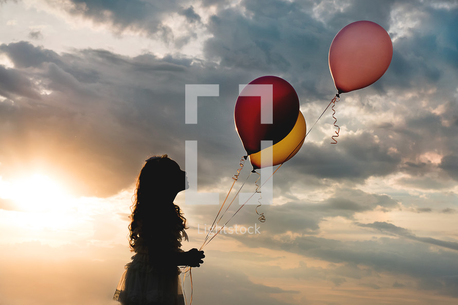 a girl child holding balloons at sunset 