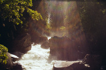 sunbeams over rocks in a river 