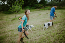 A man and woman walking their dogs through a mowed field.