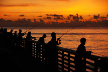 Silhouettes of men fishing off of a pier at dawn