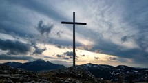 Christian cross on a rock in a mountain landscape, Dramatic clouds over the silhouette of the mountains in winter, landscape, Sun Timelapse