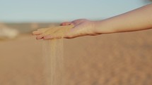 Close-up hand signs with handful of sand. Sand from the desert spills out of the girl’s hand. 4K Slow Motion
