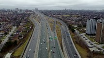 Aerial shot of a drone moving across Highway 401 in Toronto on a cloudy day. The drone is approaching a couple of road junctions that with slightly busy traffic.
