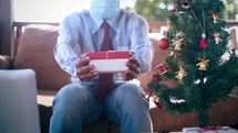 a man wearing a face mask opening a Christmas gift 