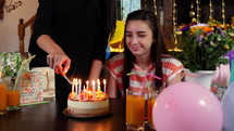 Happy teen girl with birthday cake at anniversary party. Lighting candles on birthday cake. People celebrating birthday concept. Slow motion