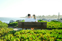 couple sitting on a park bench near the ocean 