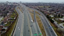 Aerial view of a drone flying over Highway 401 in Toronto on a cloudy day. The drone is moving towards a couple of road junctions that have slightly busy traffic.