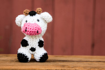 a crocheted cow in front of a red barn