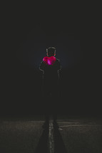 silhouette of a man holding a glowing heart standing in darkness 