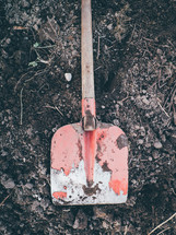A red shovel  sitting on some dirt ready to be dug
