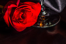 A deep red rose next to a wine glass.