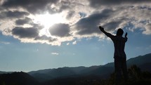 a man with hands raised standing on a mountaintop 