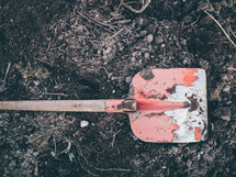 a red shovel sitting on dirt ready to be dug