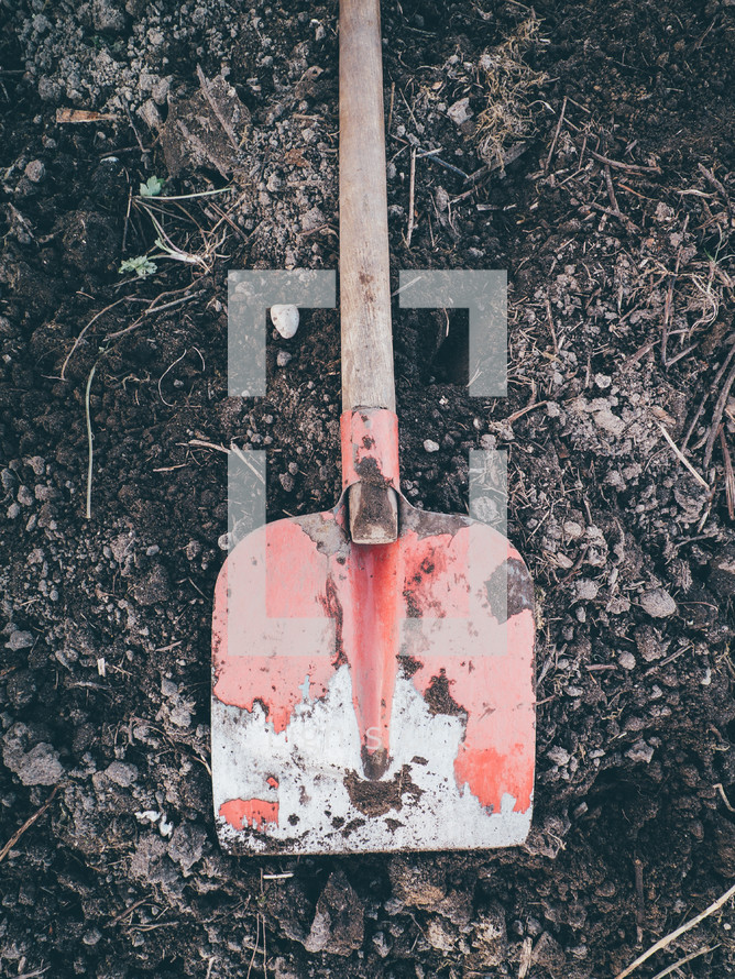 A red shovel  sitting on some dirt ready to be dug
