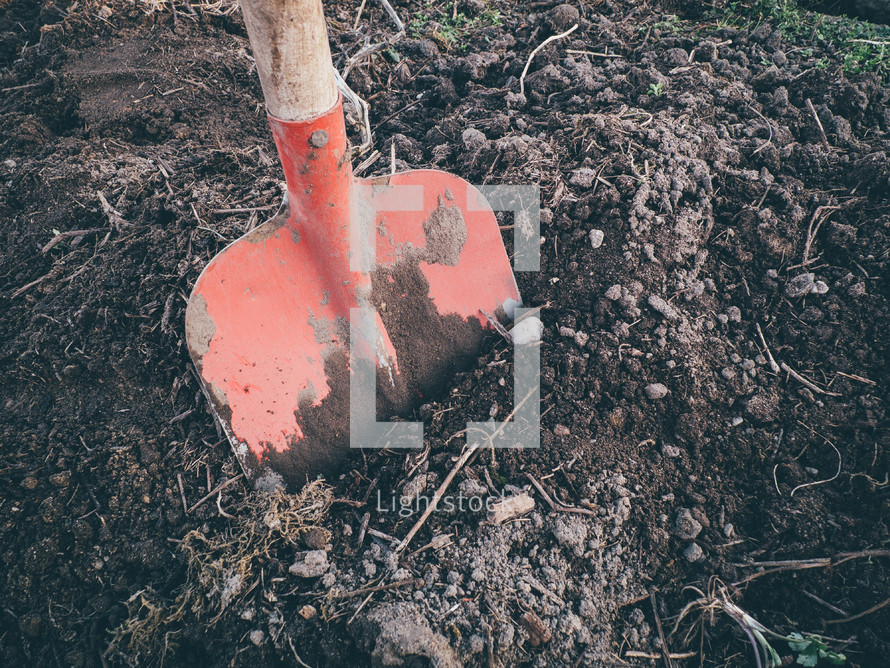 A red shovel  digging some dirt