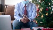 a man holding a stethoscope praying at home next to a Christmas tree 