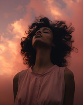A young woman looking with eyes closed head lifted toward sky during sunset