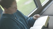 Young woman reading her Bible by a window.
