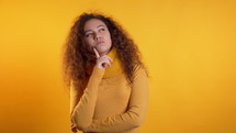 Thinking woman looking up and around on yellow background. Worried contemplative face expressions. Pretty curly haired model.