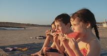 Three kids eating watermelons at the beach together