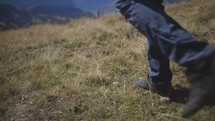 a close up of a young man's shoes and the ground as he is walking and then starting to run  through a field in the mountains