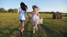 Friendly family. Mother and daughter holding hands at sunset running in the meadow. Happy mom and daughter walk holding hands towards the sunset in summer. Freedom happiness concept.