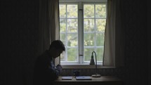 Man reading Bible at desk in front of a window with natural light
