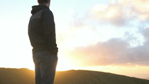 man standing on a mountaintop looking out at a sunrise 