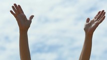 A woman raising her hands in praise on a sunny day