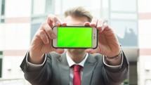 a business man holding up a cellphone with a green screen - for editorial use only 