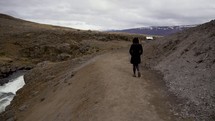 a woman in a coat walking on a dirt path 