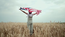 Patriot woman standing with american national flag in rural wheat field landscape. Symbol of democracy, independence, USA, 4th July celebration, US banner, memorial Veterans, election, America, labor