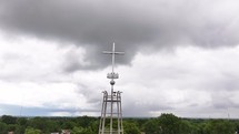 Time-lapse of moving clouds with a metal cross on top of a church on a cloudy day with trees towards the bottom of the screen.