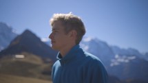 a young man walking past camera in a mountain field with epic mountains in background