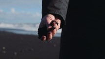 a man with a fist full of black sand standing on a beach 