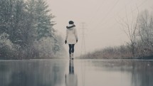 woman walking on a wet road in falling snow 