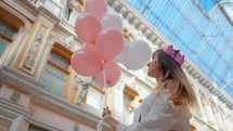 Young happy woman with colorful white and pink balloons smiling and laughing. Slow motion.