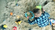 a boy child playing with sand toys in a sandbox 