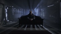 man sitting alone on a couch in a dark room 