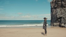a woman in a coat standing on a beach 