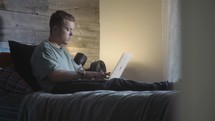 a young man sitting in bed typing on a laptop computer 