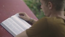 Over the shoulder close up of young man reading his Bible at a table 