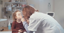 Female doctor examining a little girl's throat using an otoscope in the clinic.