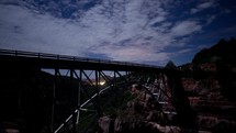 Time lapse of clouds and stars over an arched bridge crossing a canyon