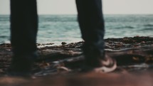 feet of a man standing on rocks on a shore 