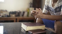 Hands folded in prayer while holding a cross on a Holy Bible.