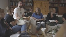 Co-ed and multi-generation community group gathered in a living room reading and discussing the Bible.