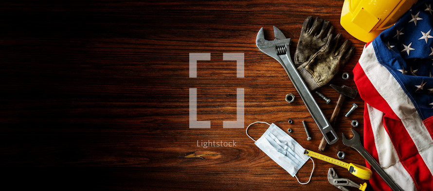 American flag, tools, hard hat, and gloves on a wood background 